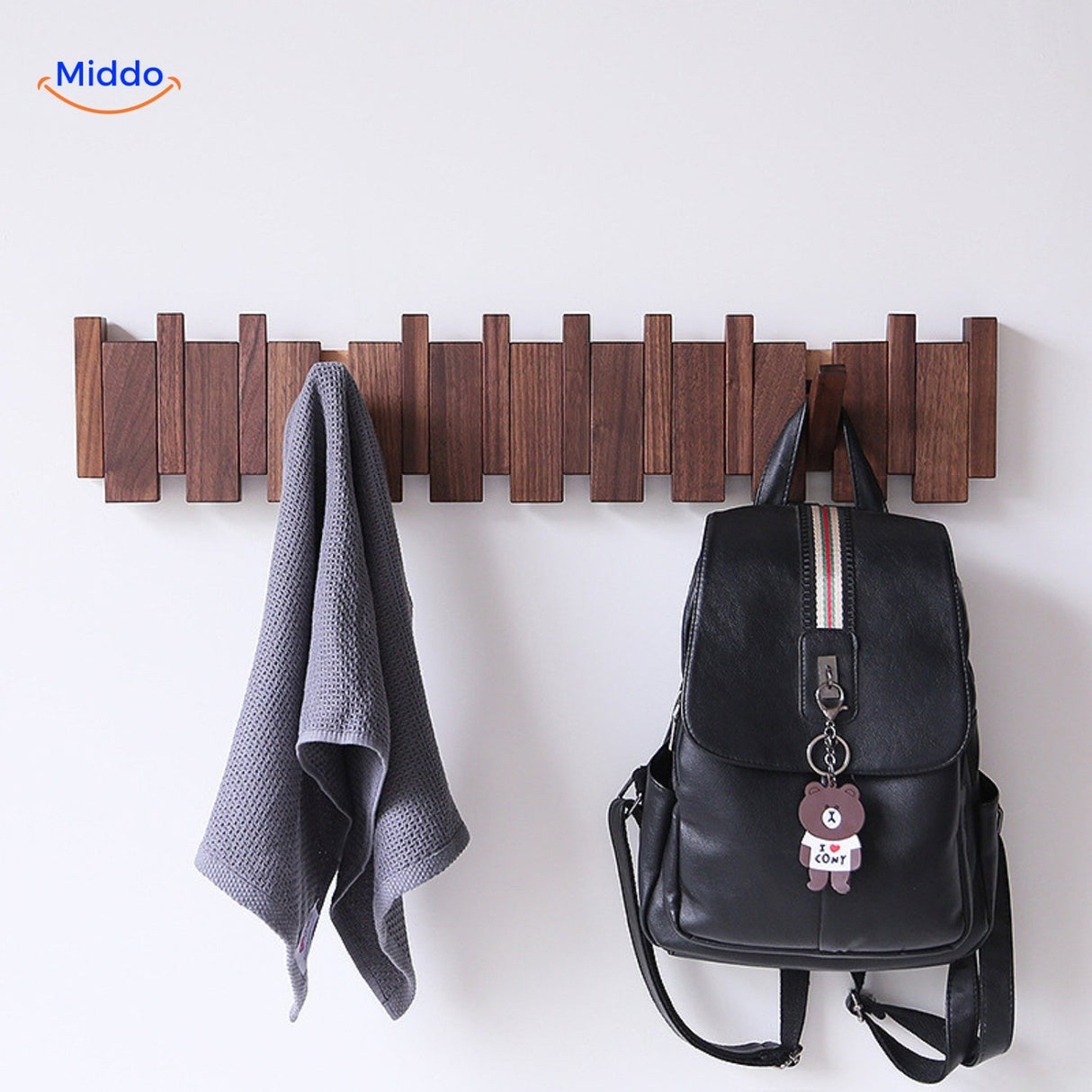 Handmade wooden piano coat rack with foldable hooks holding towels and bags on white wall.