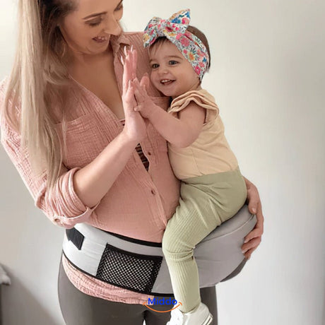 Mother wearing cream baby hip carrier while giving high-five to toddler.