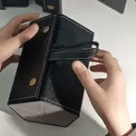 Hands demonstrating the fold-open mechanism of a black 6-slot multi-compartment eyeglasses case.