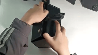Demo of a black foldable multi-compartment eyeglasses case being held by its handle, showing portability.