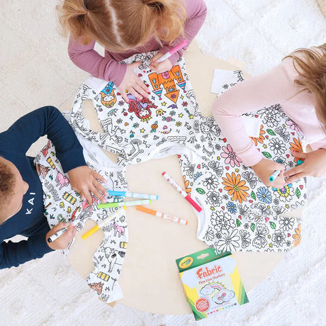 Kids sitting at table wearing color-your-own pajama and creating with markers.