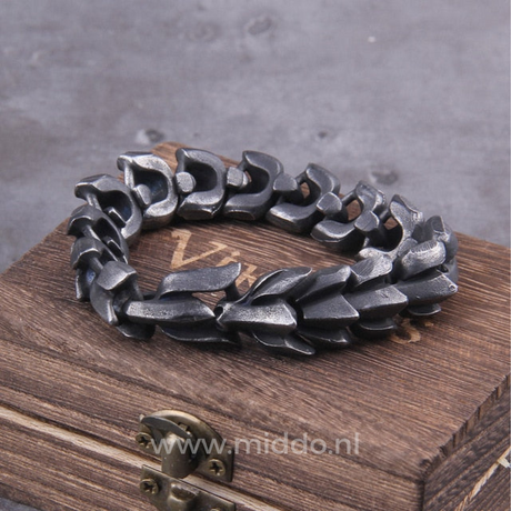 Dark silver Viking dragon bracelet displayed on a rustic wooden chest evoking Norse heritage.