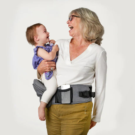 Grandmother comfortably carrying grandchild in ergonomic hip seat carrier.