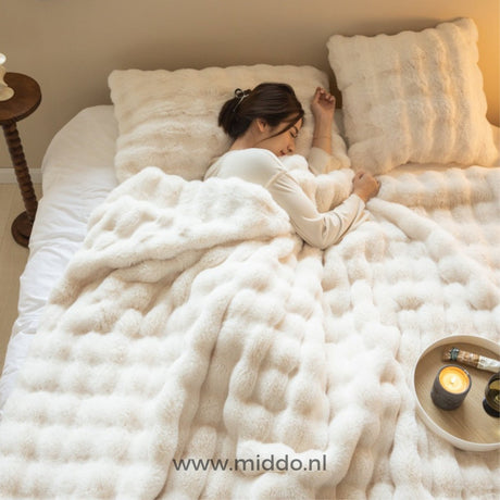 Fluffy faux fur winter blanket draped over couch in warm home setting.