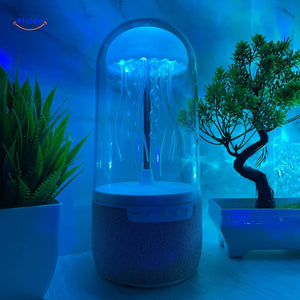 JellyGlow bluetooth speaker glowing blue with jellyfish theme on desk with decorative plants.