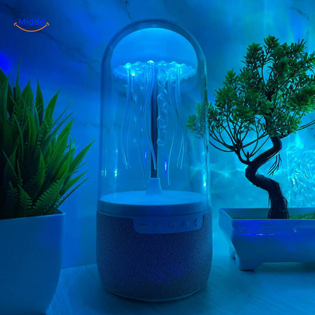 JellyGlow bluetooth speaker glowing blue with jellyfish theme on desk with decorative plants.