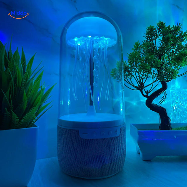 JellyGlow bluetooth speaker glowing blue with jellyfish theme on desk with decorative plants.