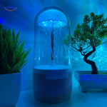 JellyGlow bluetooth speaker glowing blue with jellyfish theme on desk with decorative plants.
