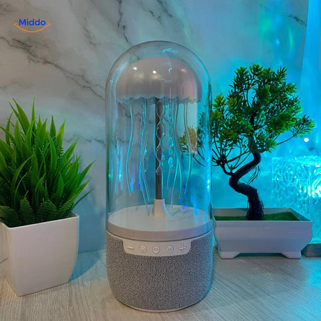 Compact JellyGlow speaker on desk with mood lighting effects and decorative plants in background.