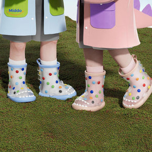 Children wearing shark rain boots styled with colorful rain jackets on outdoor terrain.