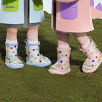 Children wearing shark rain boots styled with colorful rain jackets on outdoor terrain.