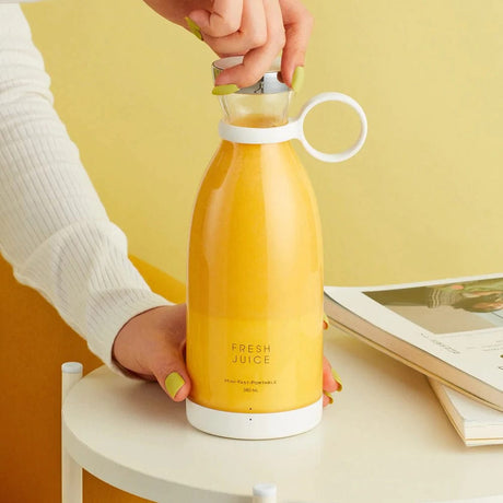 Hand holding cordless portable blender with freshly blended juice in cup.