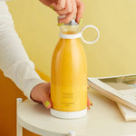 Hand holding cordless portable blender with freshly blended juice in cup.