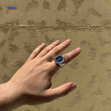 Silver ring watch with black square dial on hand model.