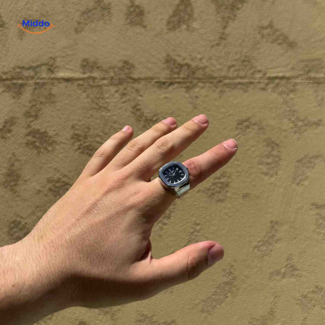 Silver ring watch with black square dial on hand model.