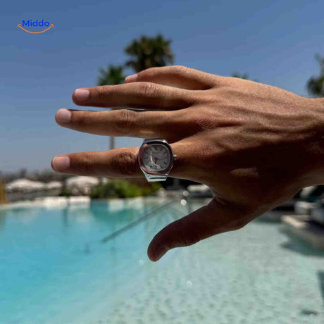 Silver ring watch with white square dial worn on finger.