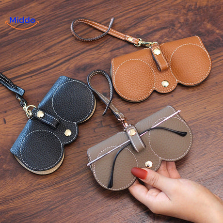 Slim leather glasses case in use protecting eyewear collection on desk.