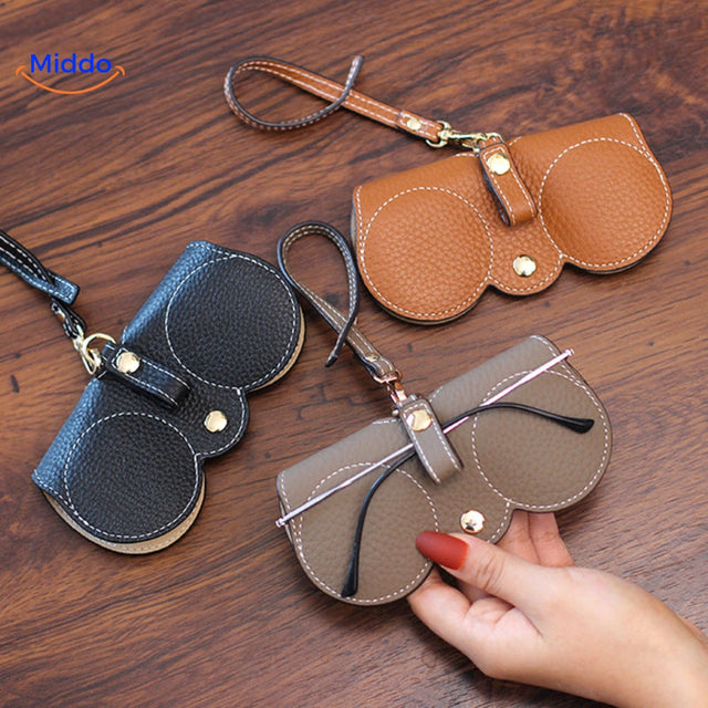 Slim leather glasses case in use protecting eyewear collection on desk.