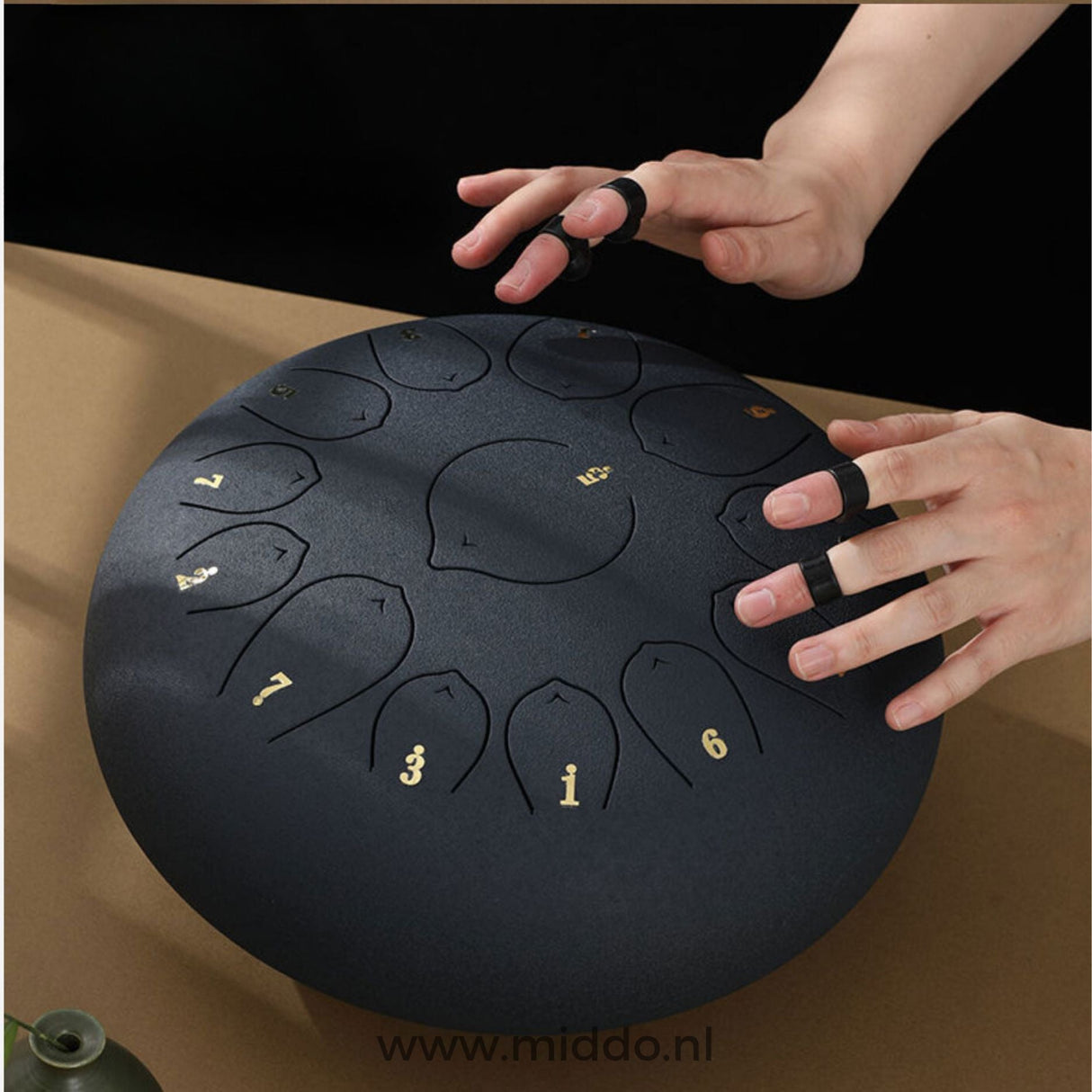 Black steel tongue drum being played with mallets in use.