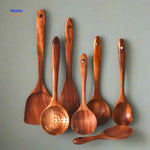 Wooden spoons and spatulas in wall-mounted teak holder for convenient kitchen access.