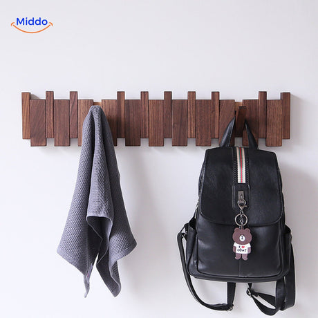 Handmade wooden piano coat rack with foldable hooks holding towels and bags on white wall.