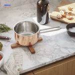 Wooden trivet in kitchen setting with copper-bottom cookware and modern decor.